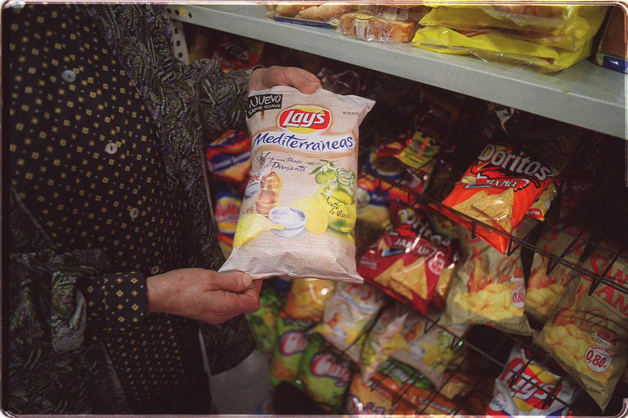 Una persona ante la estantería con patatas fritas de un supermercado.