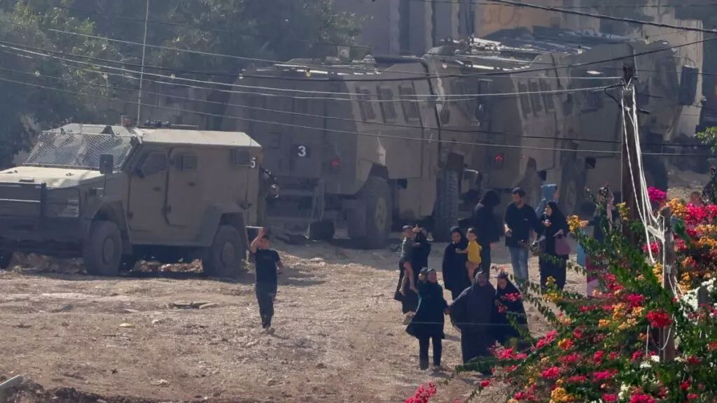 Los palestinos pasan junto a las tropas israelíes en el campo de refugiados de Yenín