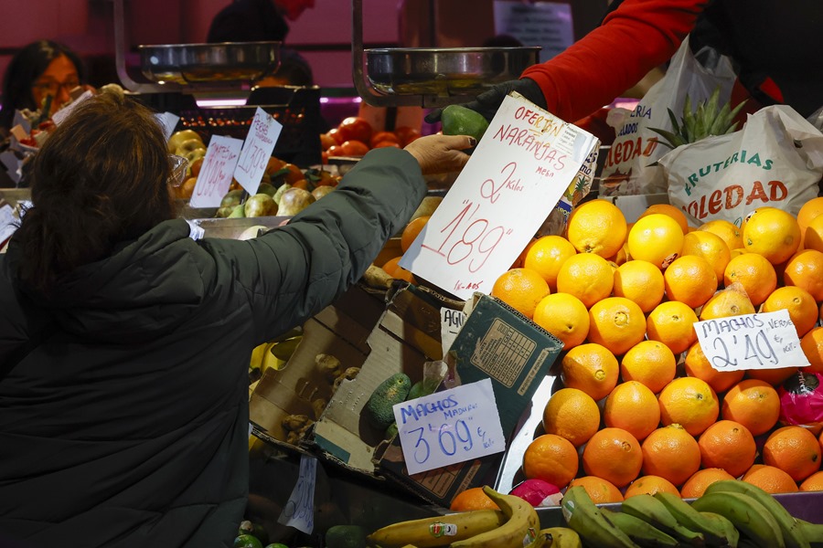 Una consumidora compra en un puesto de frutas y verduras en un mercado