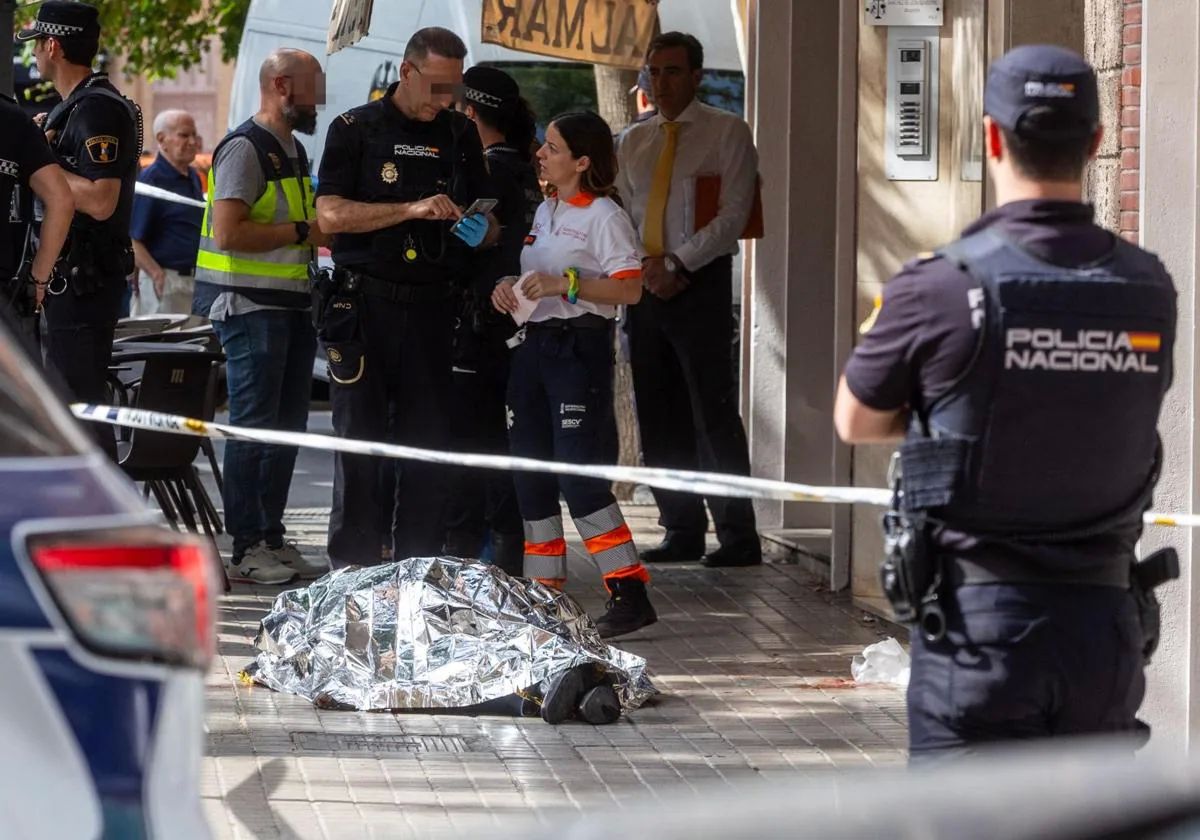 Policías y sanitarios junto al cadáver del hombre en la acera.